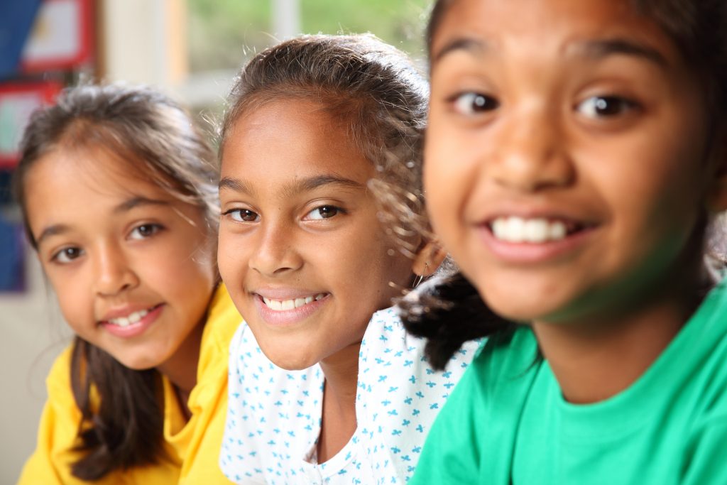 Row of three smiling young school girls sitting in class